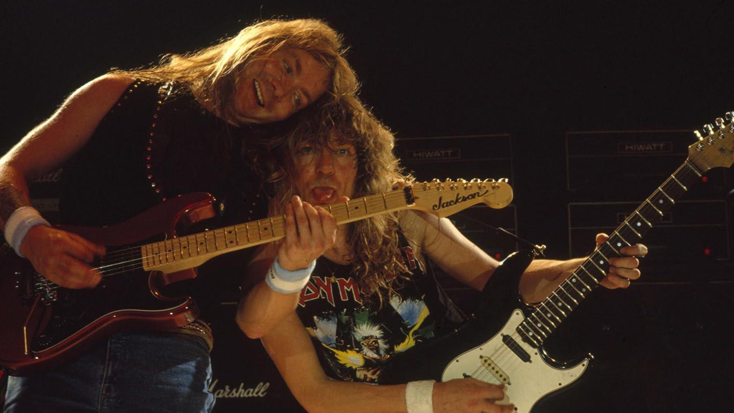 Zwei langhaarige Rockmusiker spielen auf der Bühne E-Gitarre mit Marshall- und Hiwatt-Verstärkern im Hintergrund.