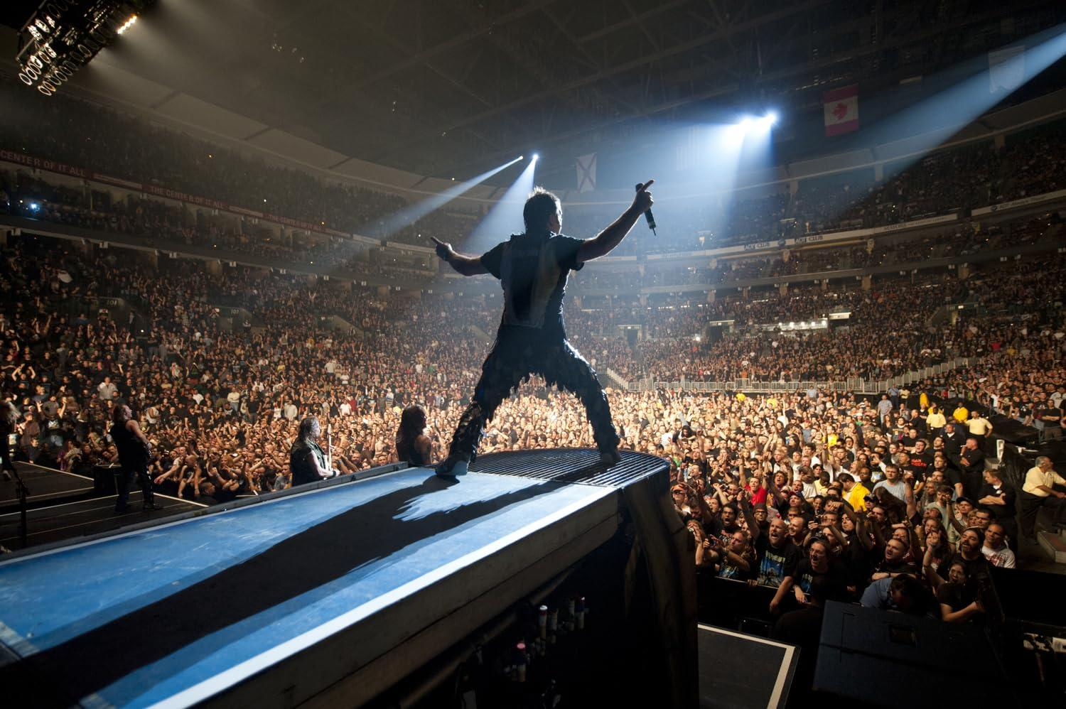 Ein Rockstar steht auf der Bühne und hält ein Mikrofon vor einer großen Menge in einer Arena.