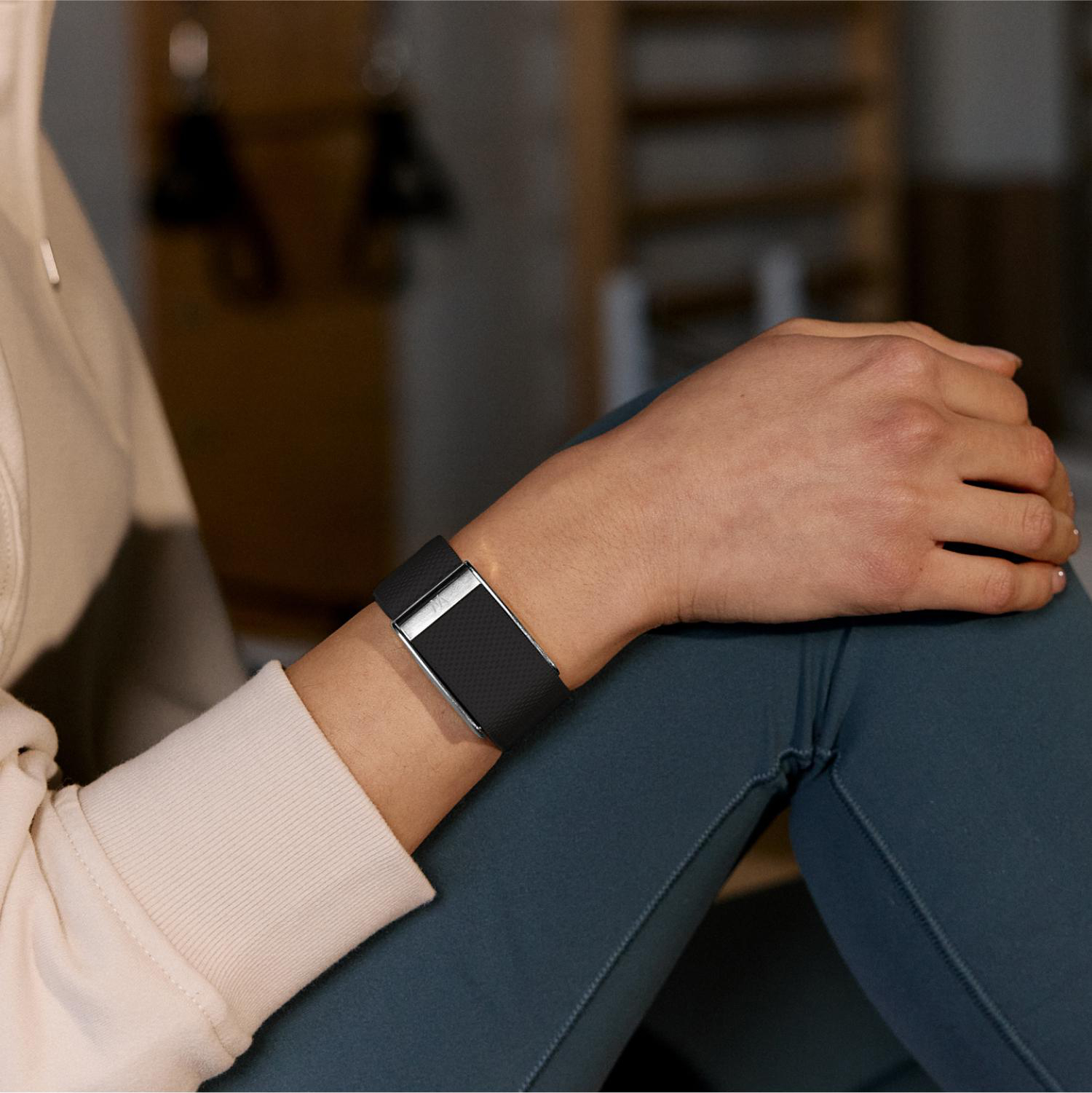 Eine Person sitzt in Sportkleidung und trägt ein schwarzes Fitnessarmband am Handgelenk.