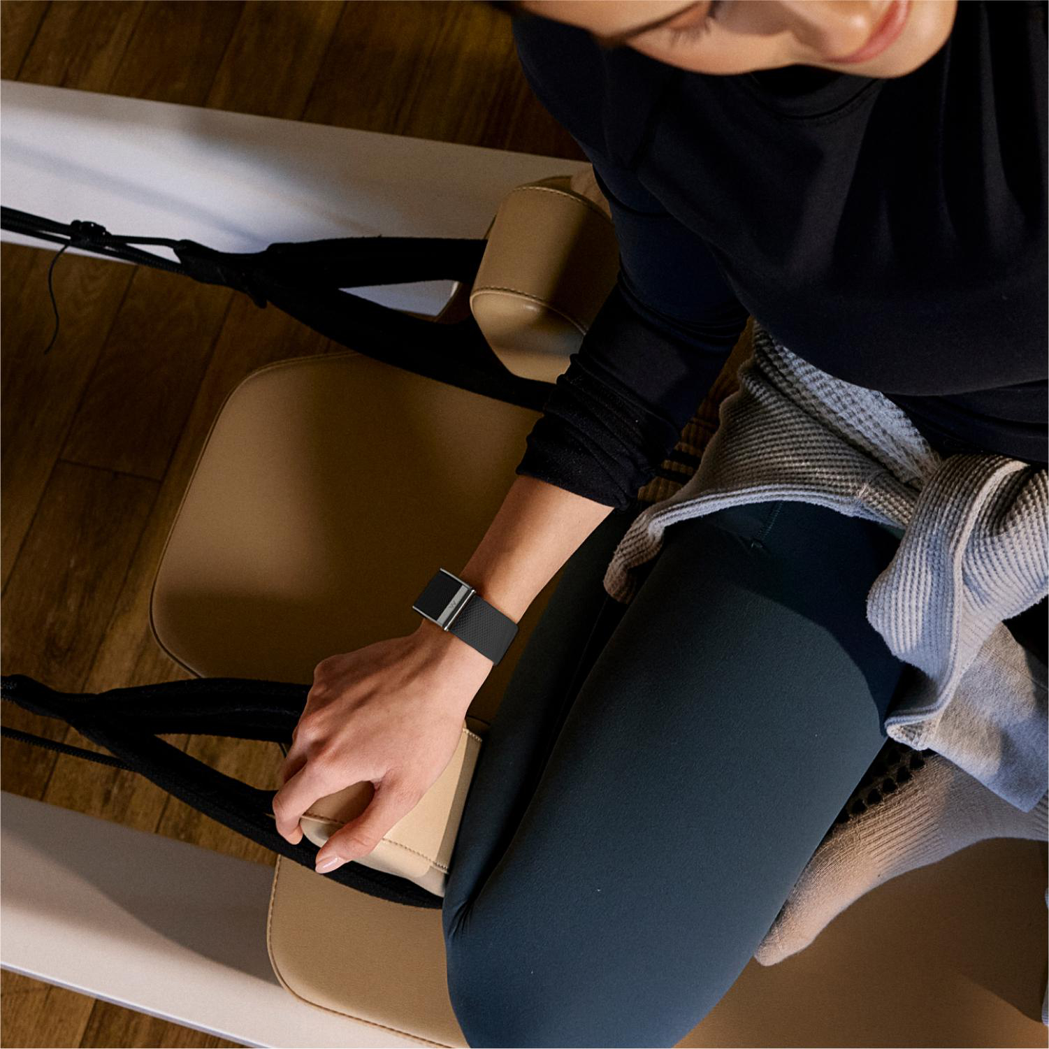 Eine Frau in Sportkleidung sitzt auf einem Pilates-Gerät und hält die Gurte.