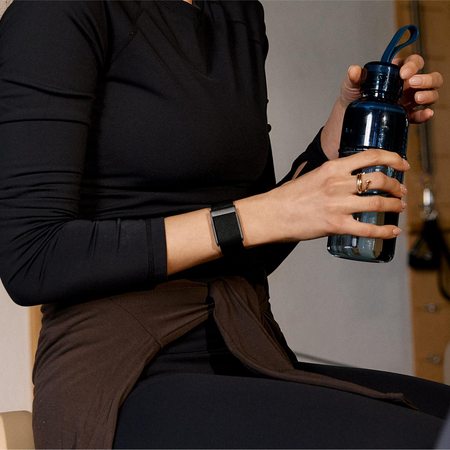 Eine Frau in schwarzer Sportkleidung hält eine blaue Trinkflasche und trägt ein Fitnessarmband.