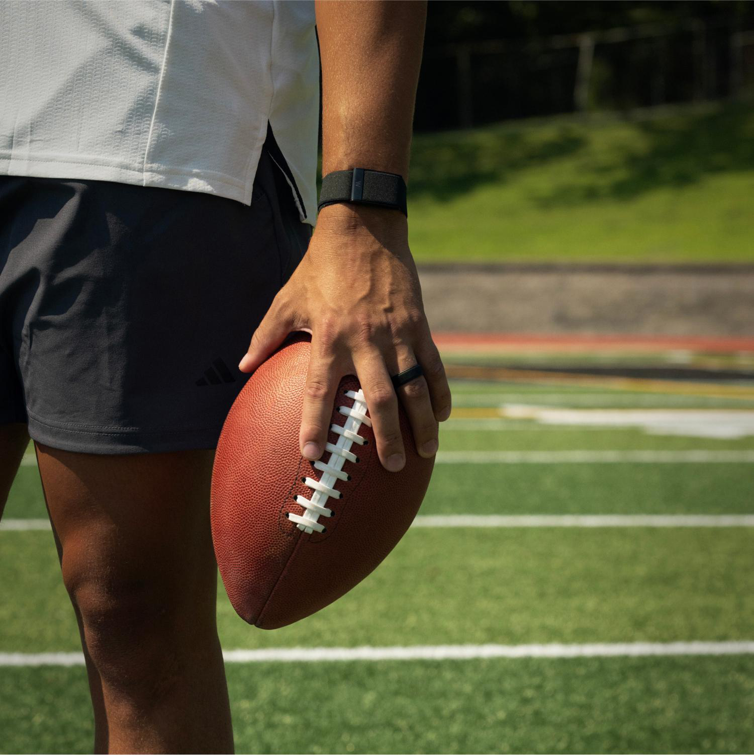 Eine Person mit Sportkleidung hält einen American Football auf einem Spielfeld.