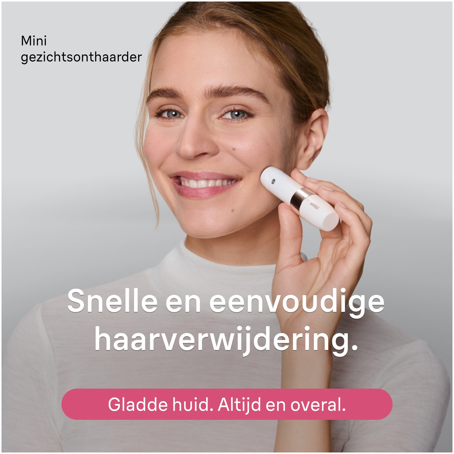 Une femme blonde utilise un petit épilateur facial blanc sur sa joue sur un fond gris.