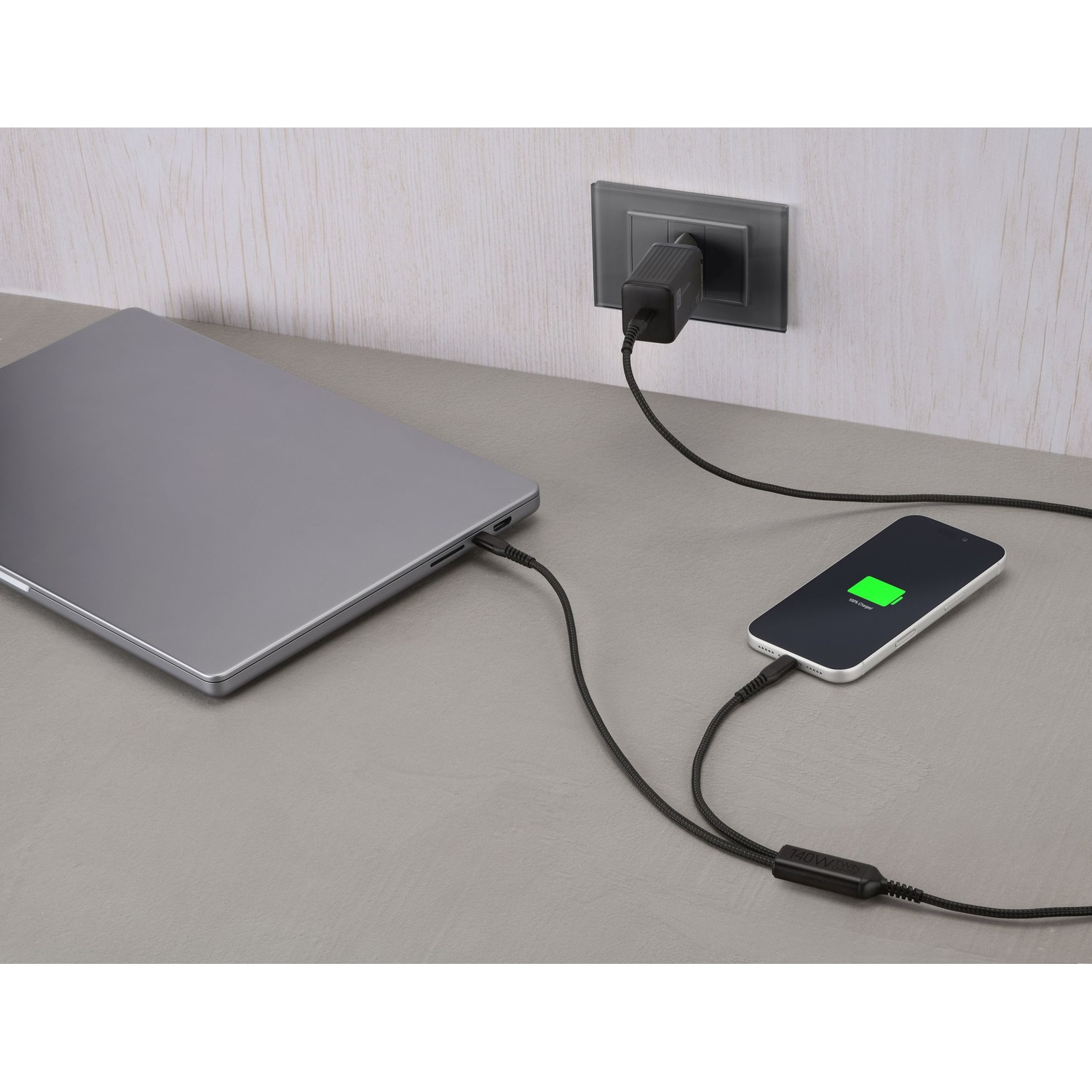 Un laptop e uno smartphone in carica su una superficie grigia con un cavo nero.