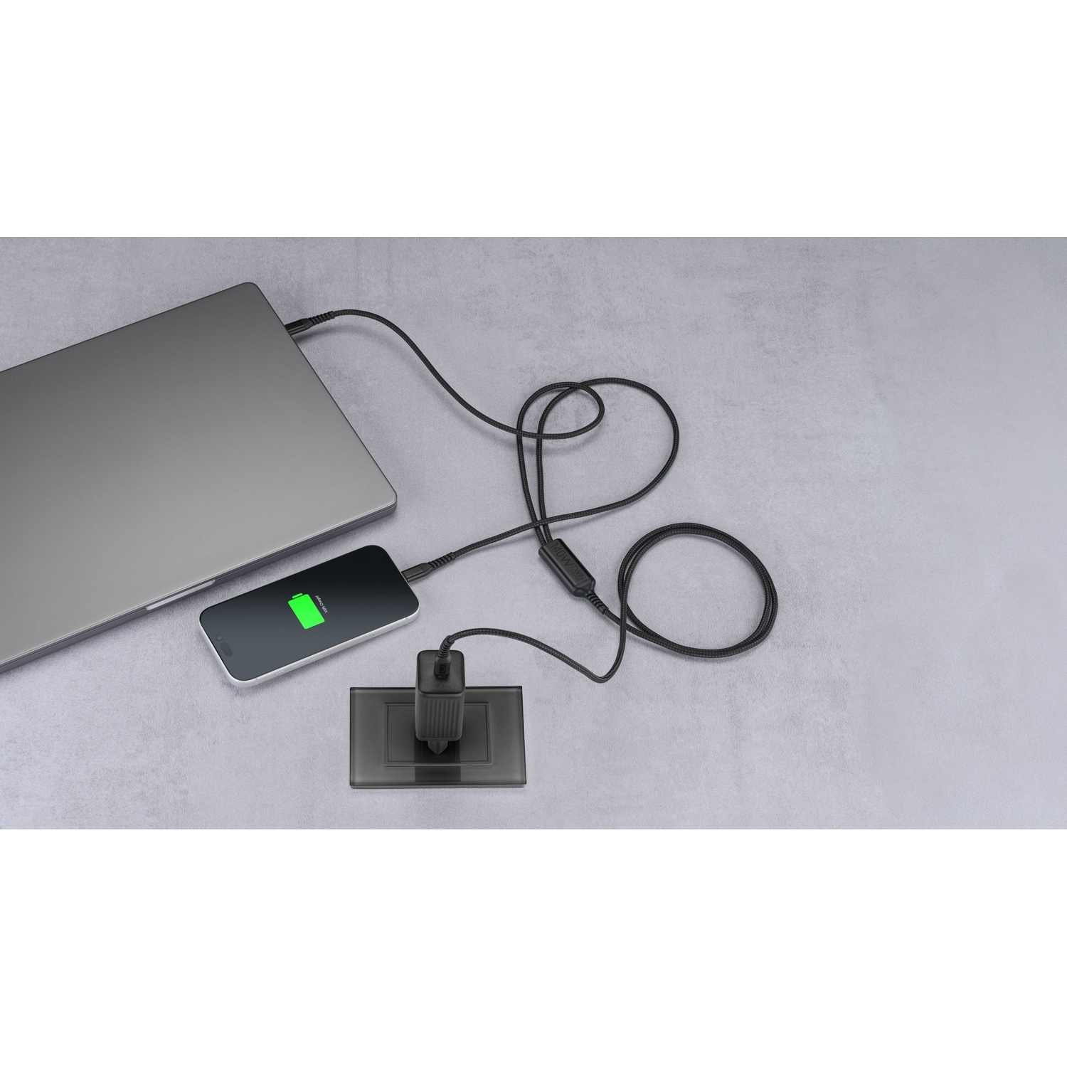 Un laptop e un telefono in carica su una superficie grigia tramite un cavo USB-C multiplo a muro.