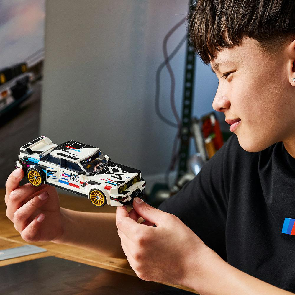 Ein junger Mann hält und bewundert ein detailliertes weißes LEGO BMW Modellauto mit bunten Aufklebern.