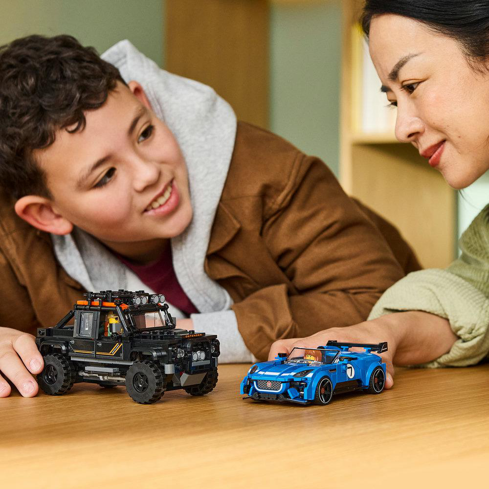 Ein Junge und eine Frau spielen mit zwei LEGO-Spielzeugautos auf einem Holztisch.