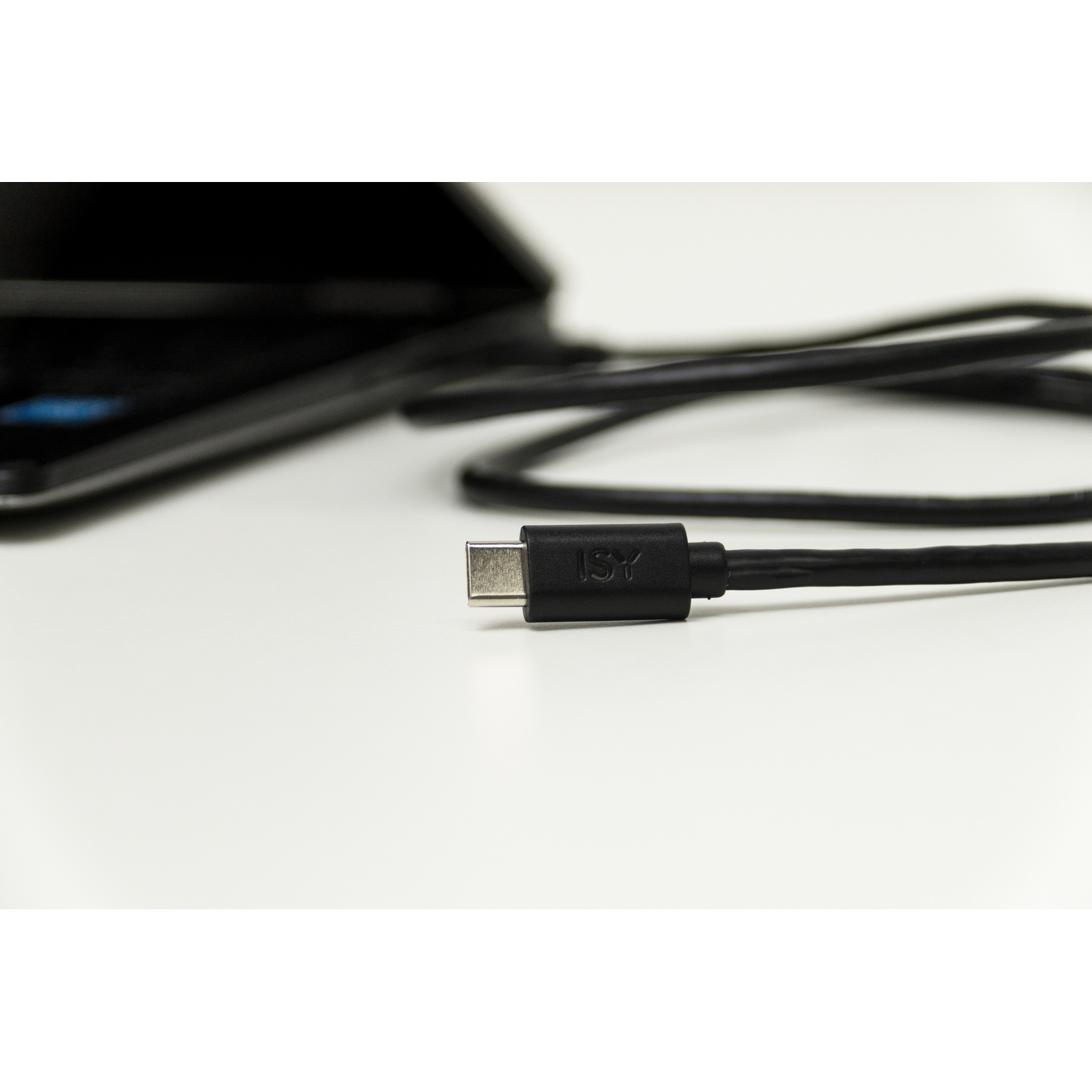 Un cavo USB-C ISY nero su una superficie chiara, con una tastiera sullo sfondo.