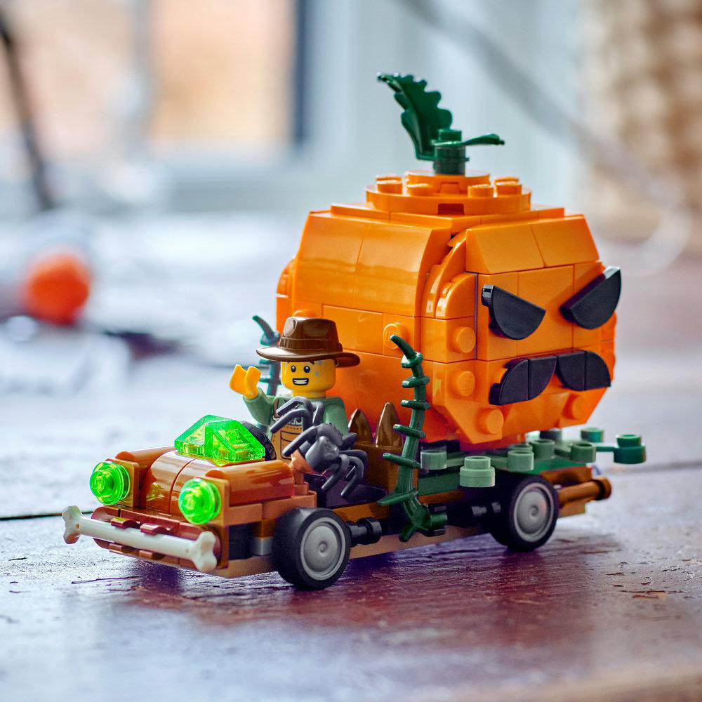 Ein Lego-Figur fährt ein Auto, das einen großen Kürbis transportiert, auf einer Holzbeschichtung.