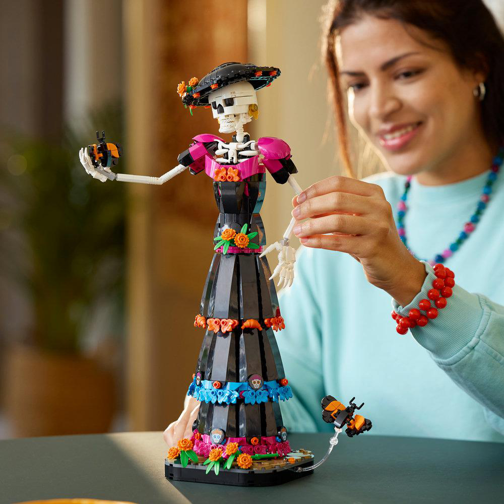 Eine Frau baut eine detailreiche LEGO Skelettfigur im traditionellen Kostüm.