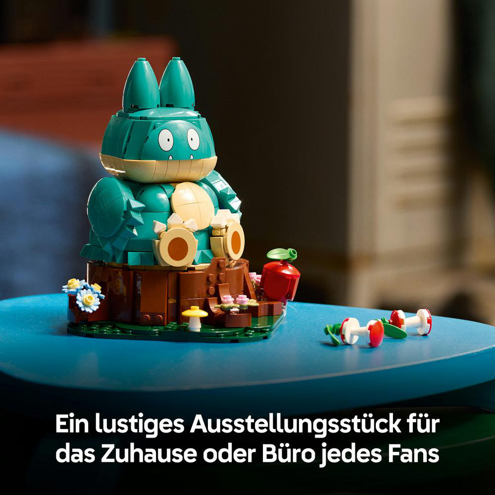 Eine Lego-Figur auf einem Baumstumpf mit Blumen auf blauem Tisch, Text unten.