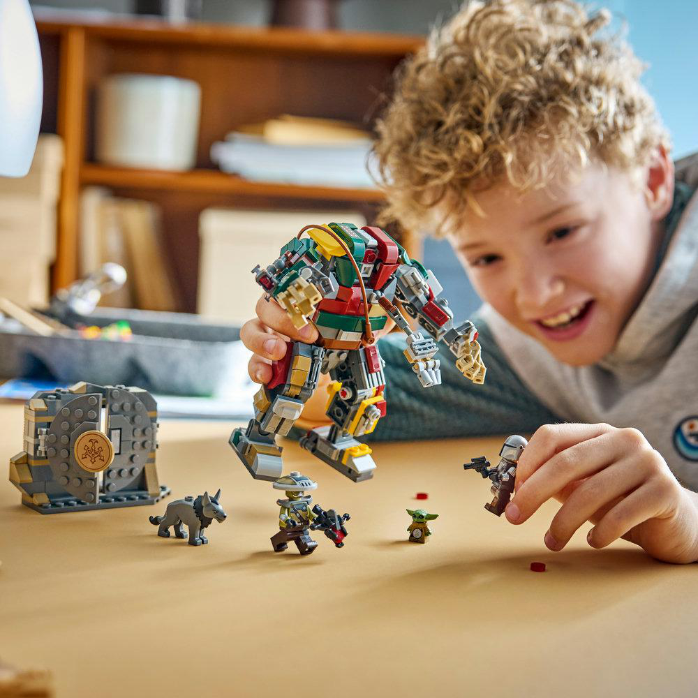 Ein Junge spielt mit Lego Star Wars Figuren und einem Mech auf einem Holztisch.