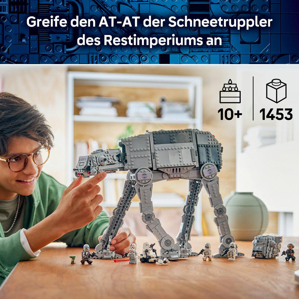 Ein Junge baut ein großes graues Lego Star Wars AT-AT Modell mit Minifiguren auf einem Holztisch.