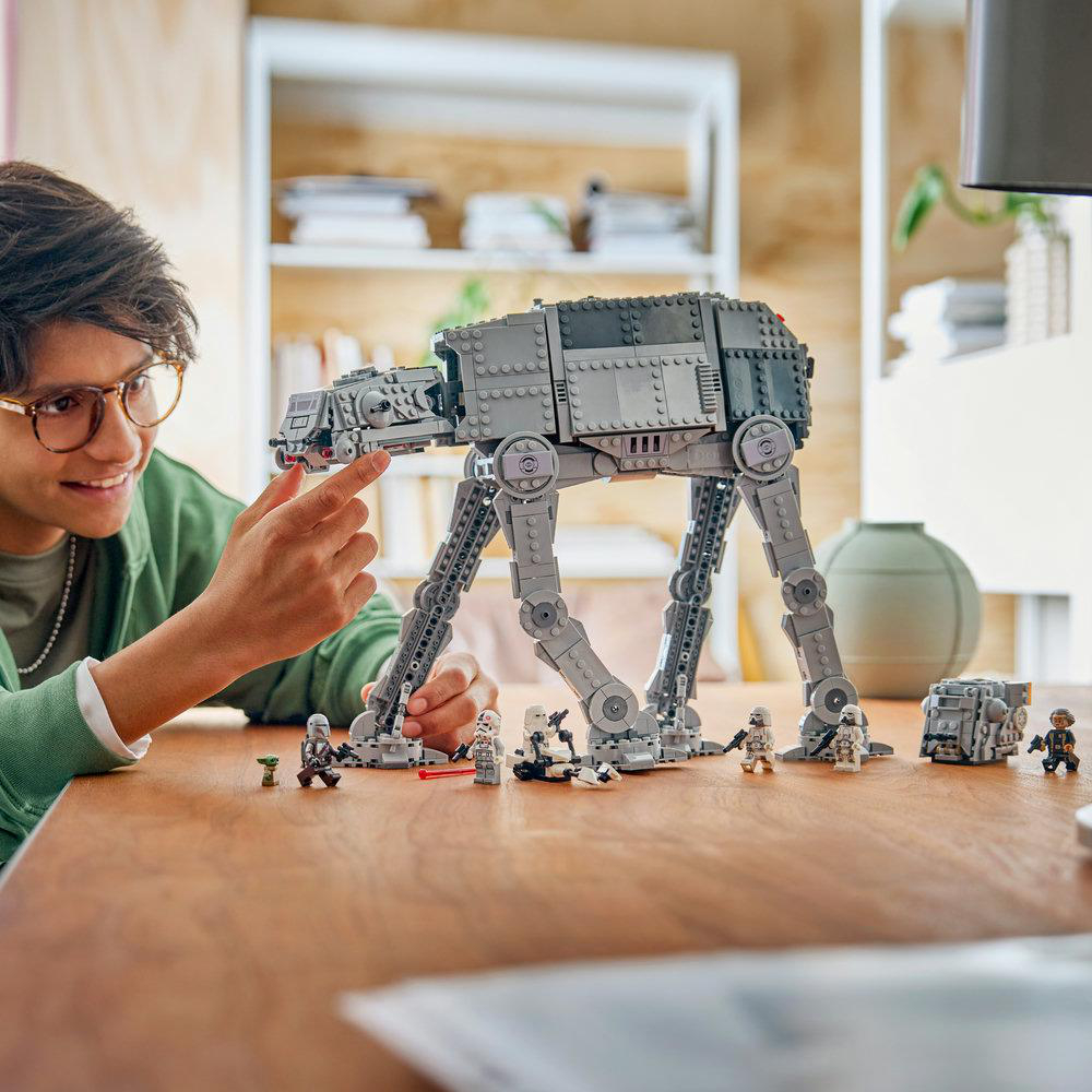 Ein Junge lächelt, während er einen großen grauen Lego Star Wars AT-AT Walker auf einem Holztisch baut.