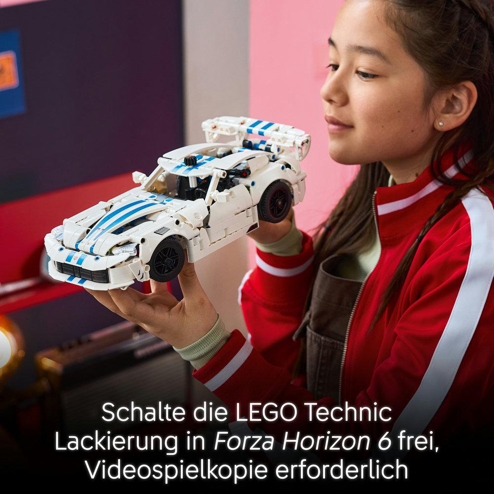 Ein junges Mädchen in einer roten Jacke hält ein weiß-blaues Lego Technic Rennauto mit deutschem Text.