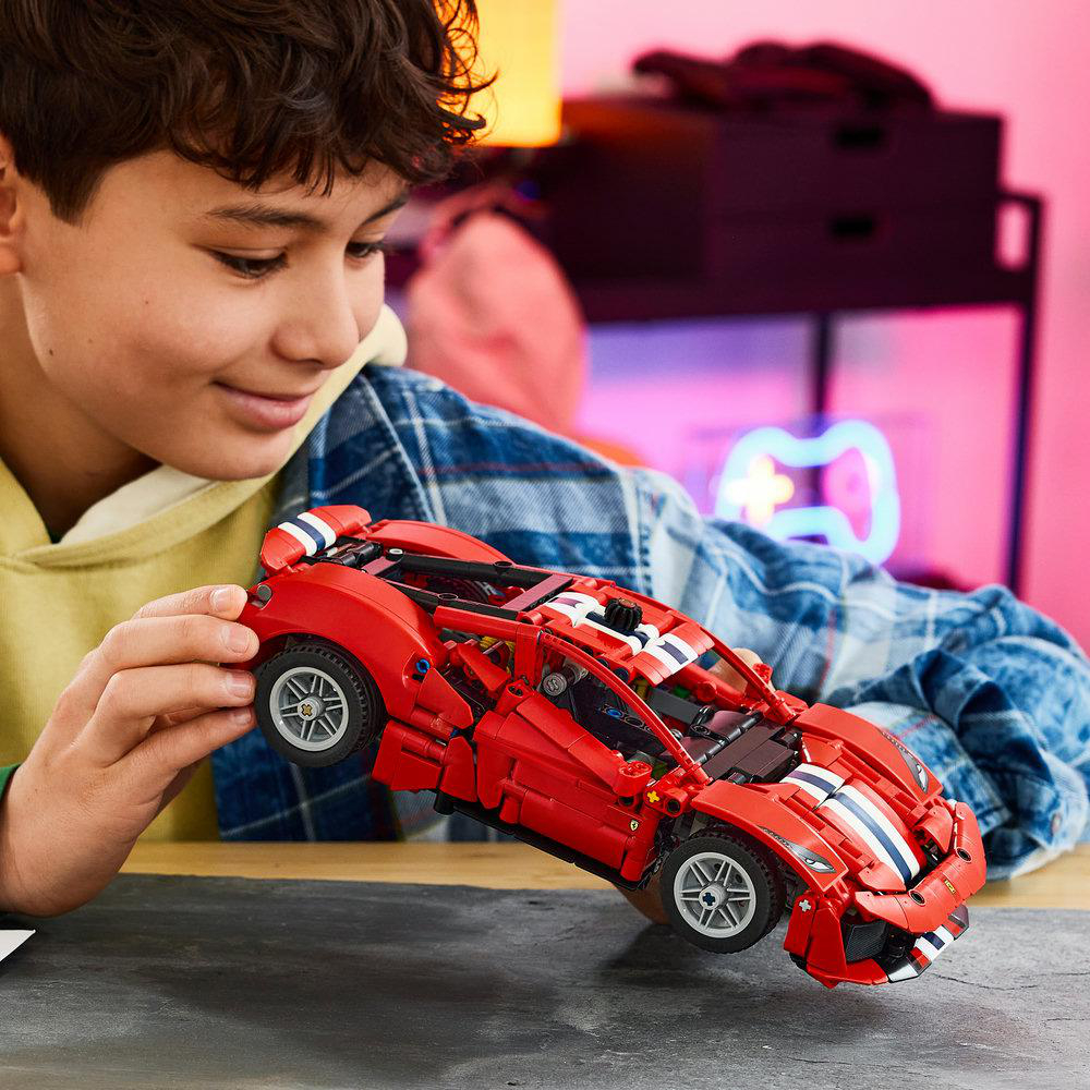 Ein Junge baut und betrachtet ein rotes Lego-Technic-Spielzeugauto in seinem Zimmer.