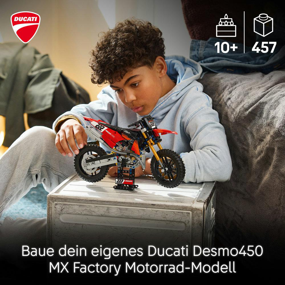 Ein Junge baut ein rotes Lego Ducati Motorrad auf einer Kiste.