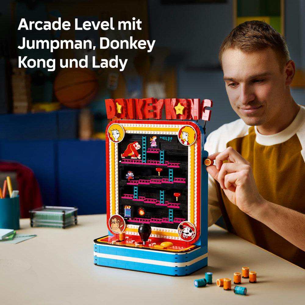 Ein Mann baut ein farbenfrohes Lego Donkey Kong Arcade-Spielmodell auf einem Tisch zusammen.