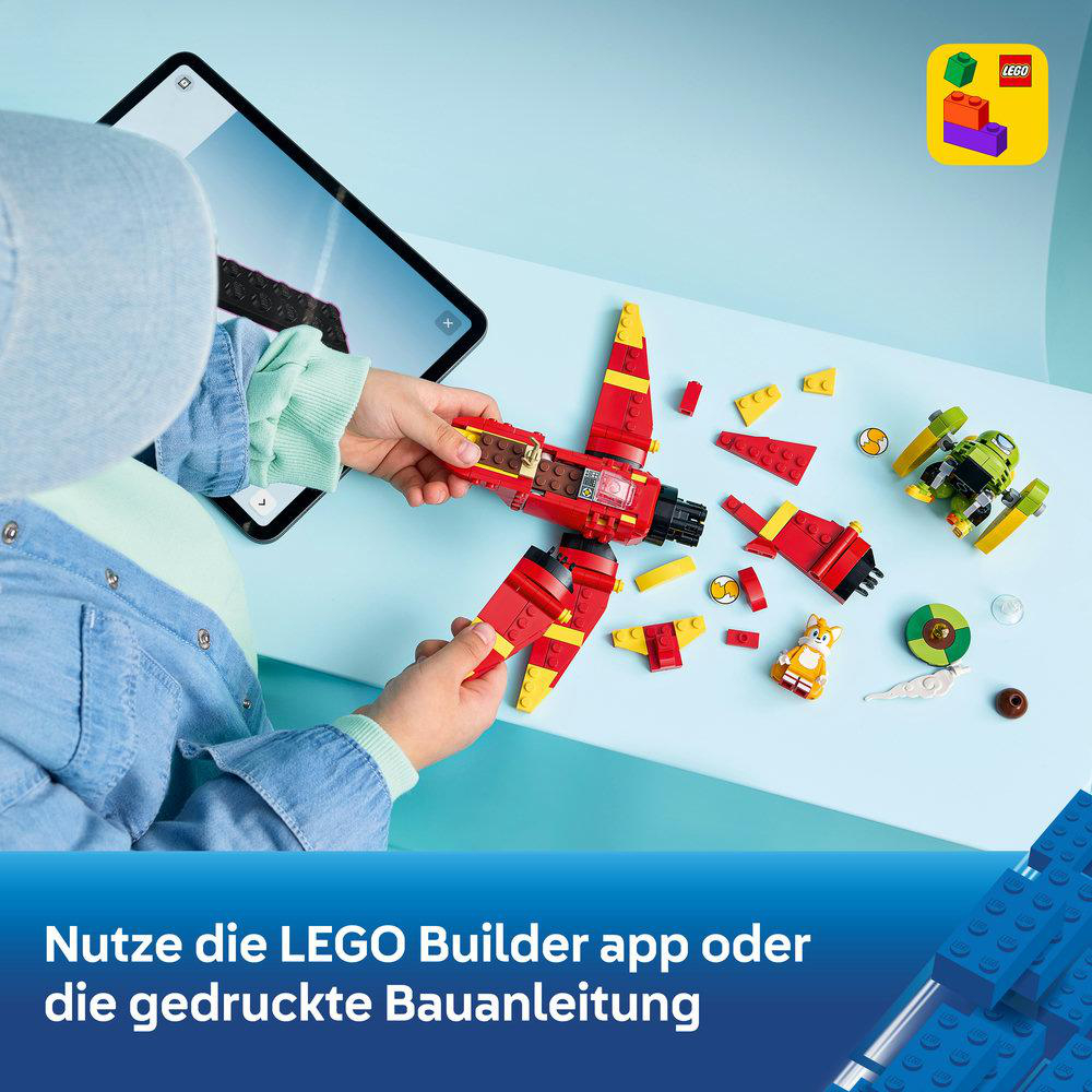 Ein Kind baut ein rotes Lego-Flugzeug neben einer Tablet-App und anderen Legoteilen.