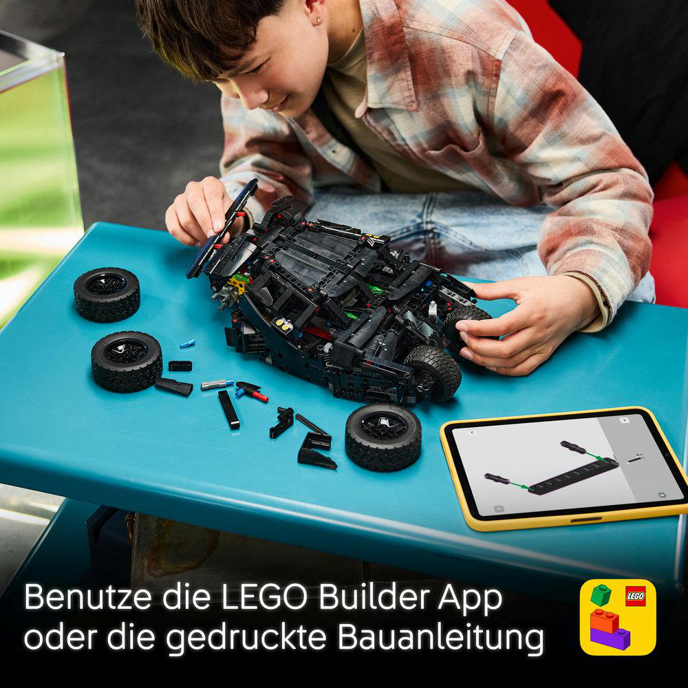 Ein Kind baut ein schwarzes LEGO Auto auf einem blauen Tisch, neben einem Tablet mit Anleitung.