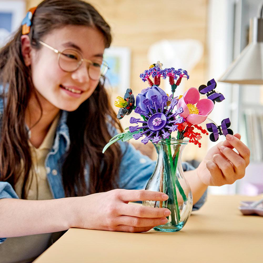 Ein lächelndes Mädchen baut einen farbenfrohen Lego-Blumenstrauß in einer Vase.