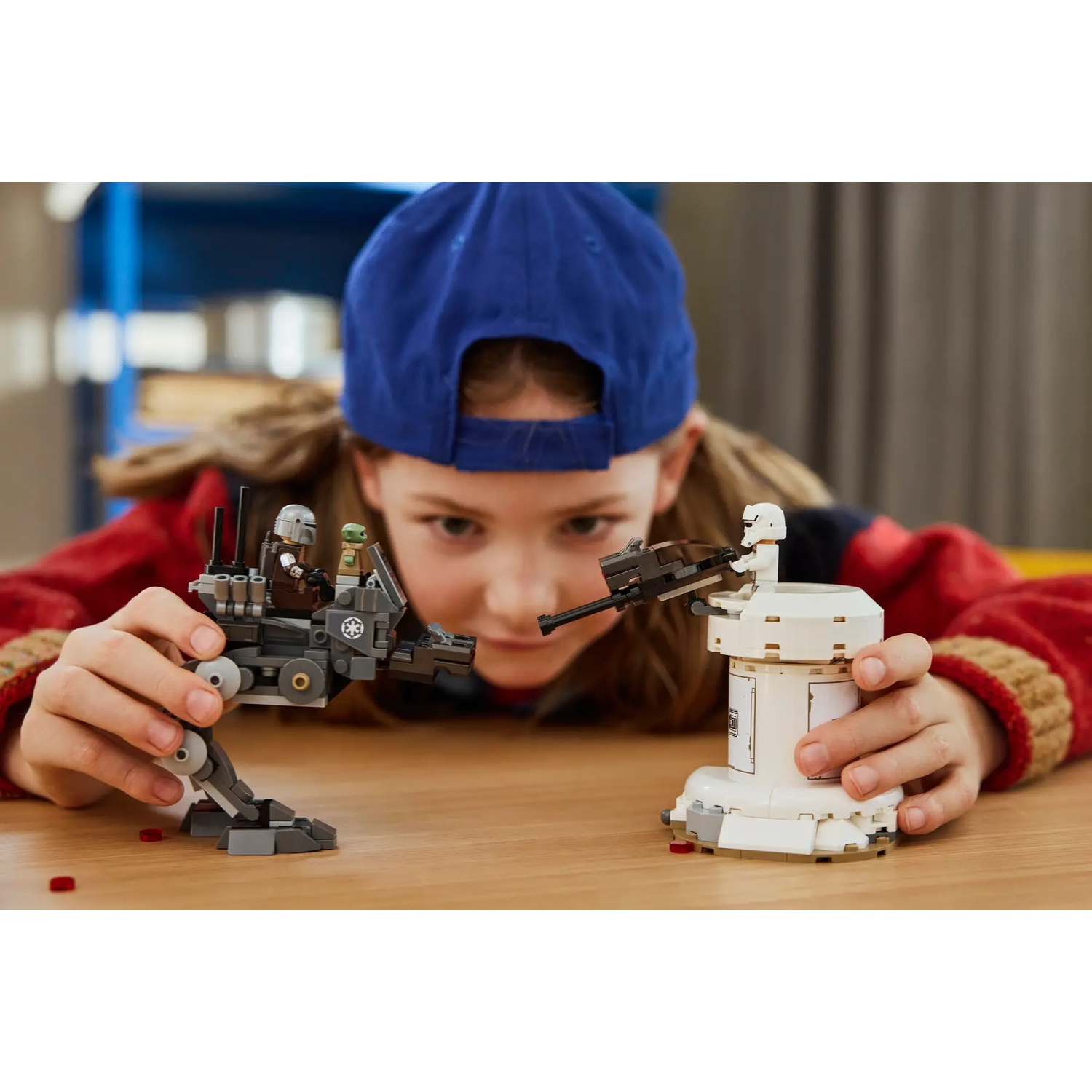 Un bambino con un berretto blu gioca con le figure e le costruzioni LEGO Star Wars su un tavolo di legno.