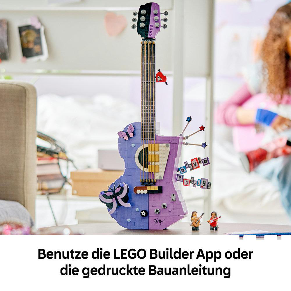 Eine violette LEGO Gitarre steht auf einem Tisch, verziert mit Sternen, Herzen und zwei kleinen Figuren daneben.