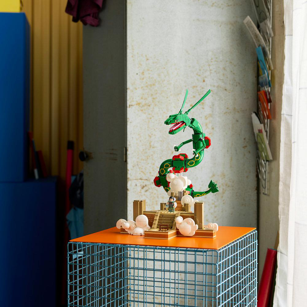 Ein grüner Lego-Drache thront auf einer Steinstruktur mit Wolken auf einem blauen Metallhocker.