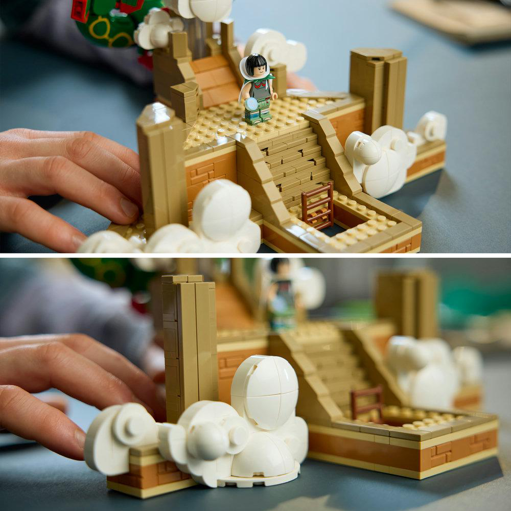 Nahaufnahme von Händen, die ein Lego-Set mit Minifigur, Steintreppe und weißen Wolkenmodellen bauen.