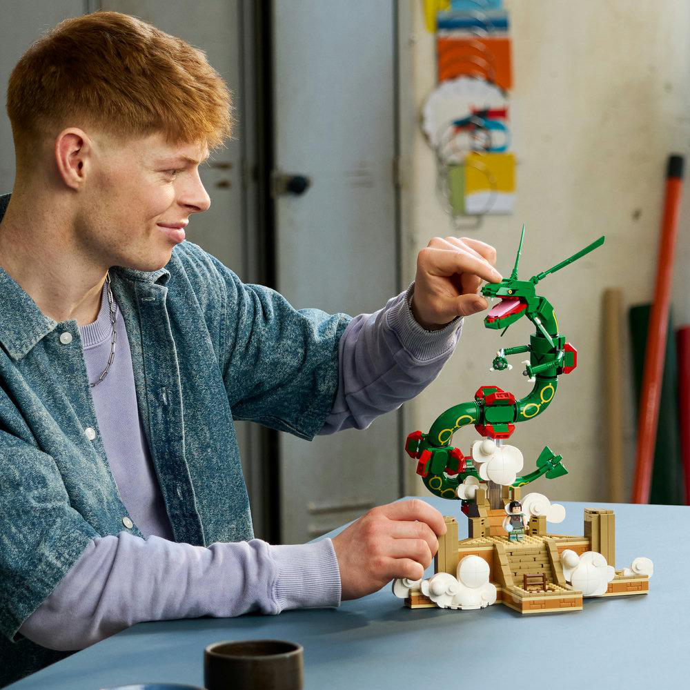 Ein junger Mann mit rotem Haar im Jeanshemd baut einen grünen Lego-Drachen auf einem Tisch.