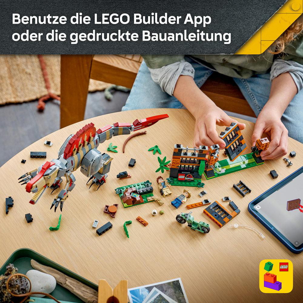 Ein Kind baut ein Lego-Jurassic-Park-Set mit einem großen Dinosaurier und kleineren Bauteilen an einem Tisch auf.