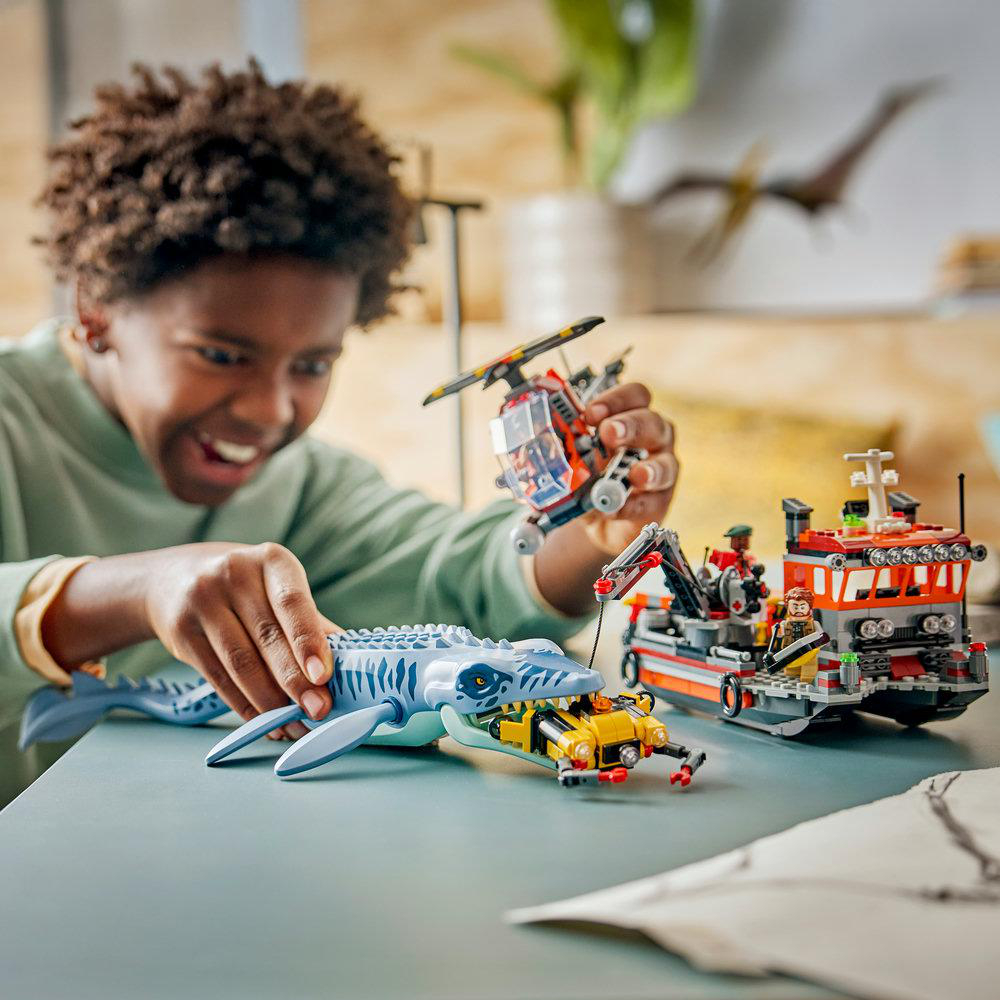 Ein lächelnder Junge spielt mit Lego-Meeresrettungssets, darunter ein Spielzeugboot, Hubschrauber und ein blaues Meerestier.
