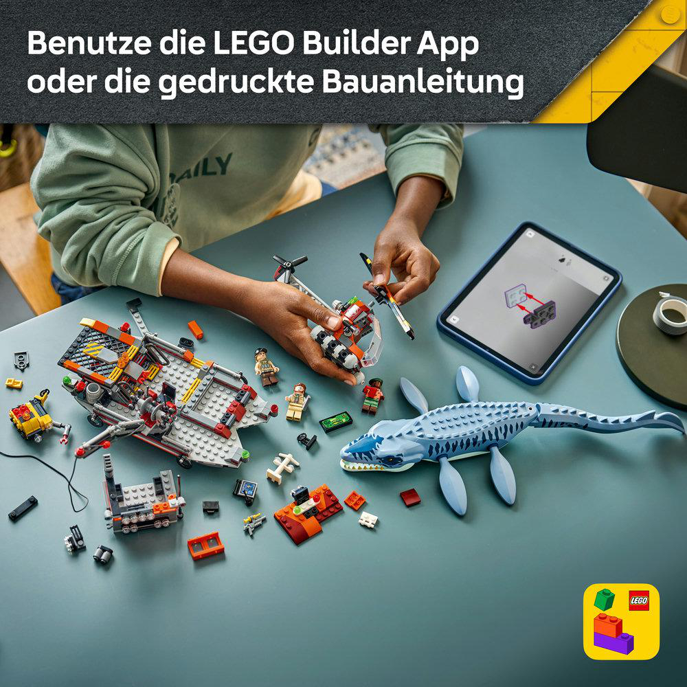 Person baut Lego-Modelle am Tisch, daneben ein Tablet mit Anleitung und ein blauer Meeresreptil-Lego.