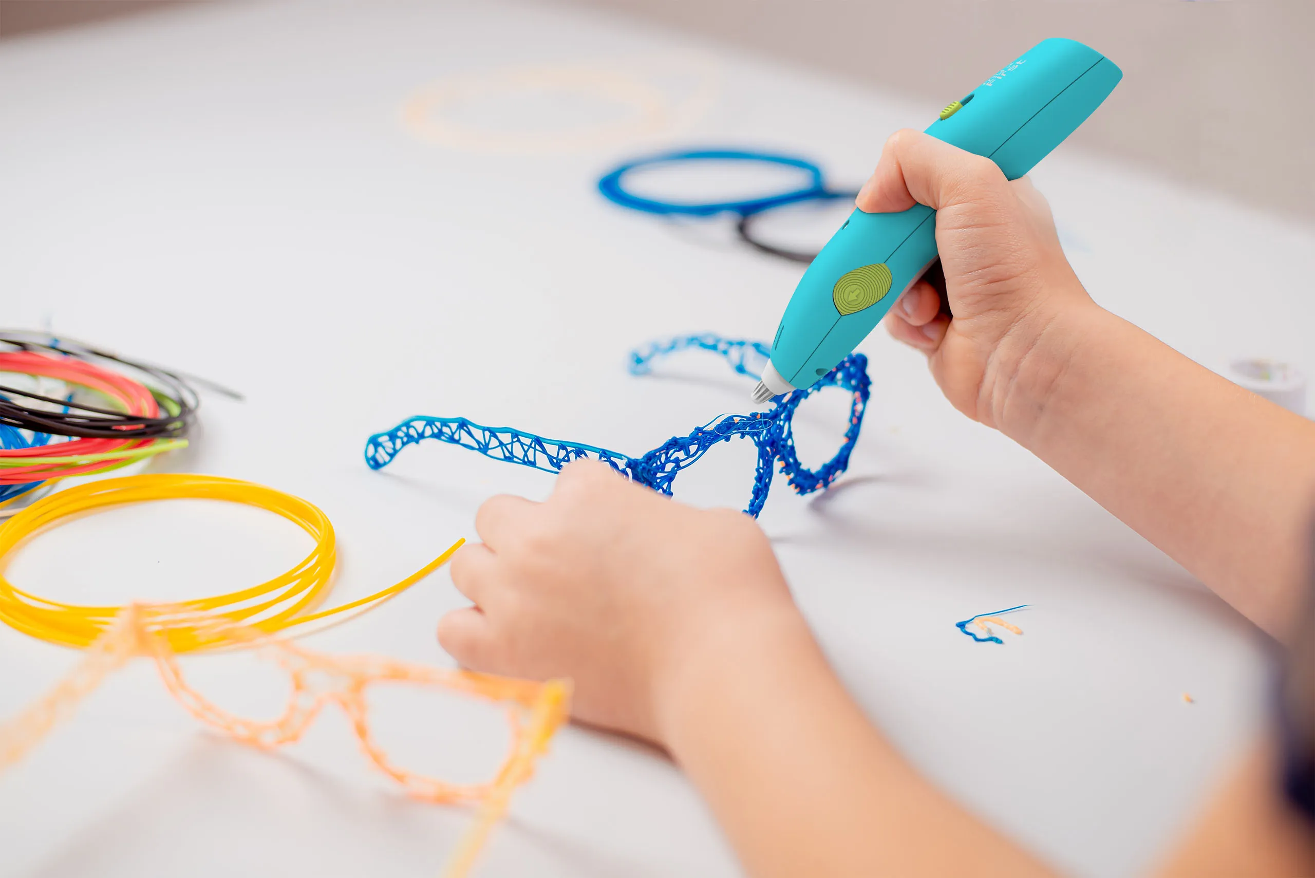 Ein Kind nutzt einen blauen 3D-Stift, um blaue Brillen aus Kunststoff auf einem Tisch zu formen.