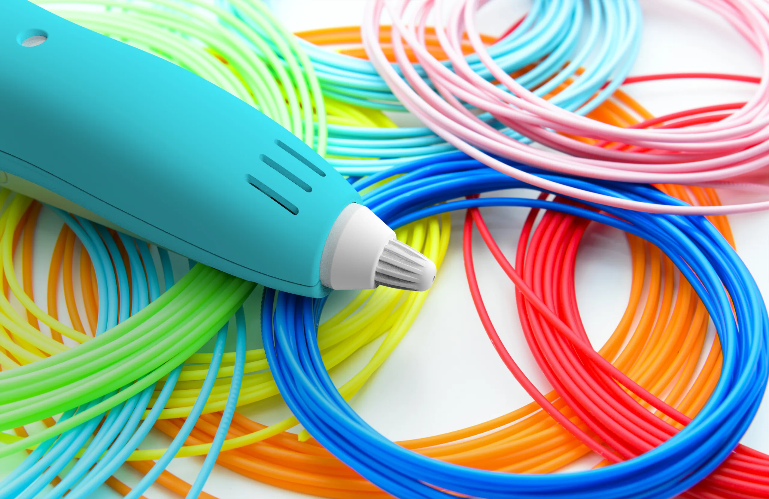 Ein türkisfarbener 3D-Druckstift auf bunten Filament-Spulen in Blau, Rot, Grün und Orange.