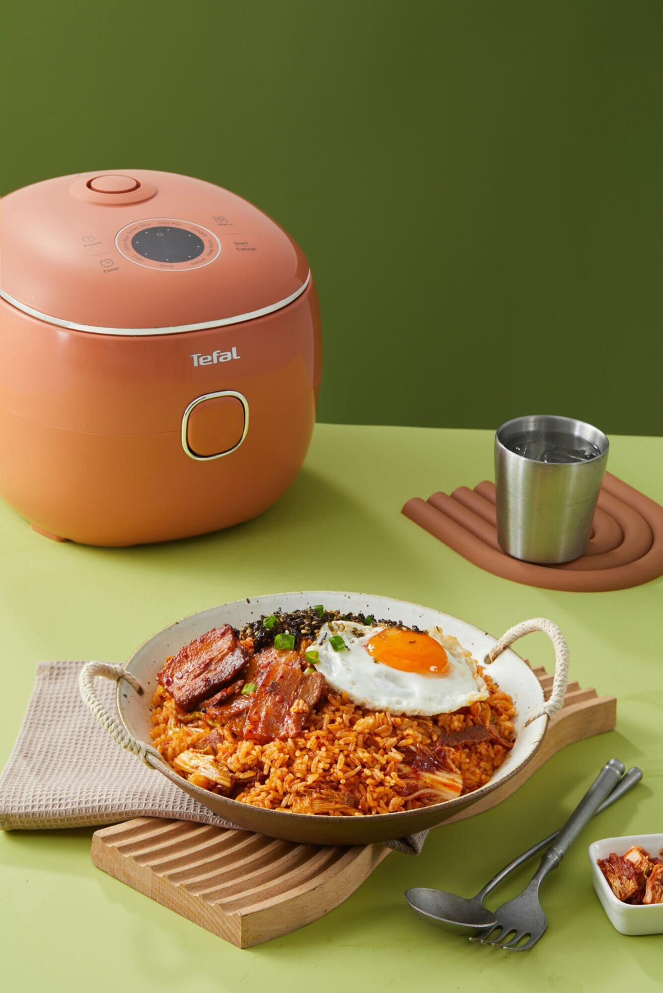 Pomarańczowy ryżowar Tefal i smażony ryż z kimchi i jajkiem sadzonym na zielonym stole.