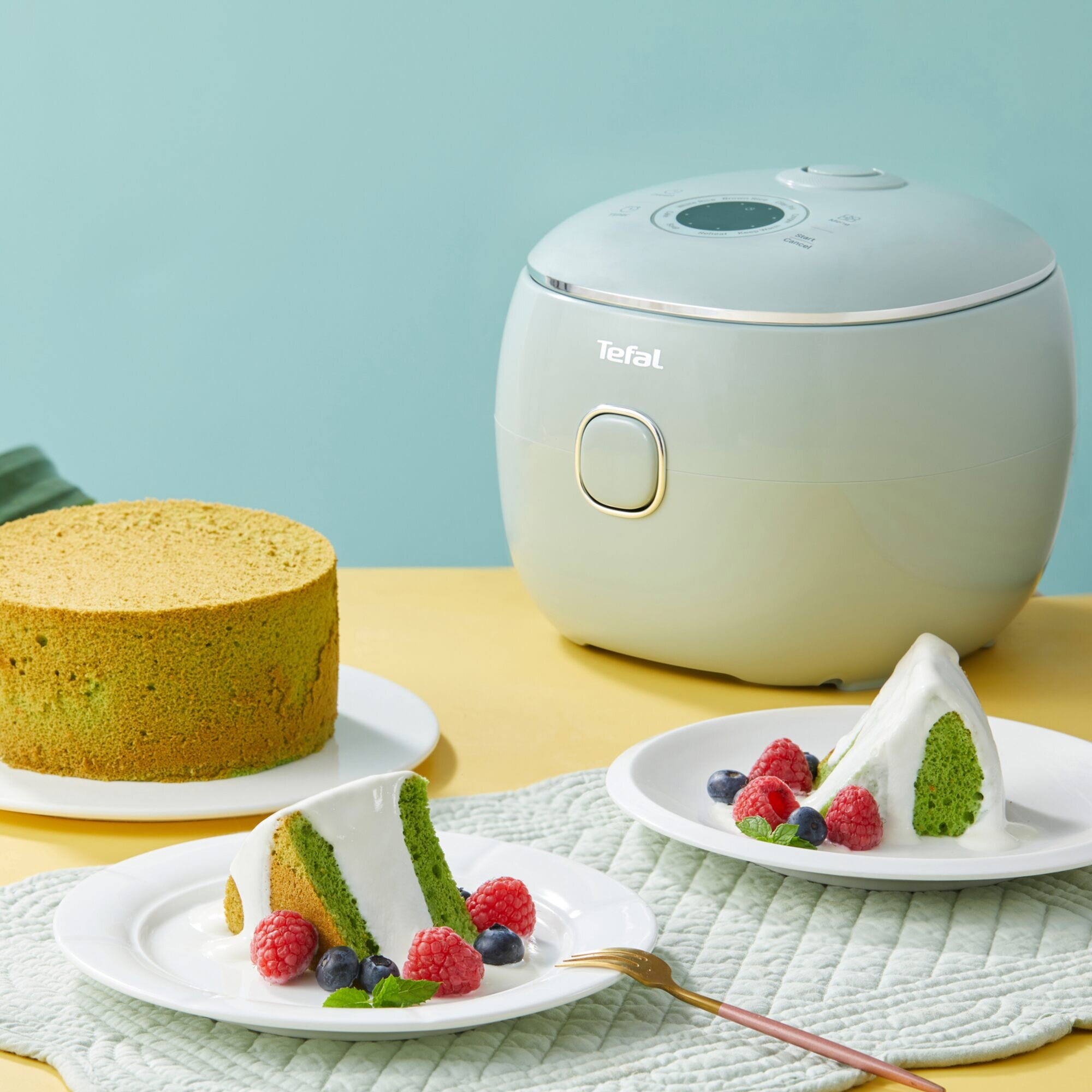 Zielone ciasto, kawałki z śmietanką i owocami oraz miętowy ryżowar Tefal na stole.