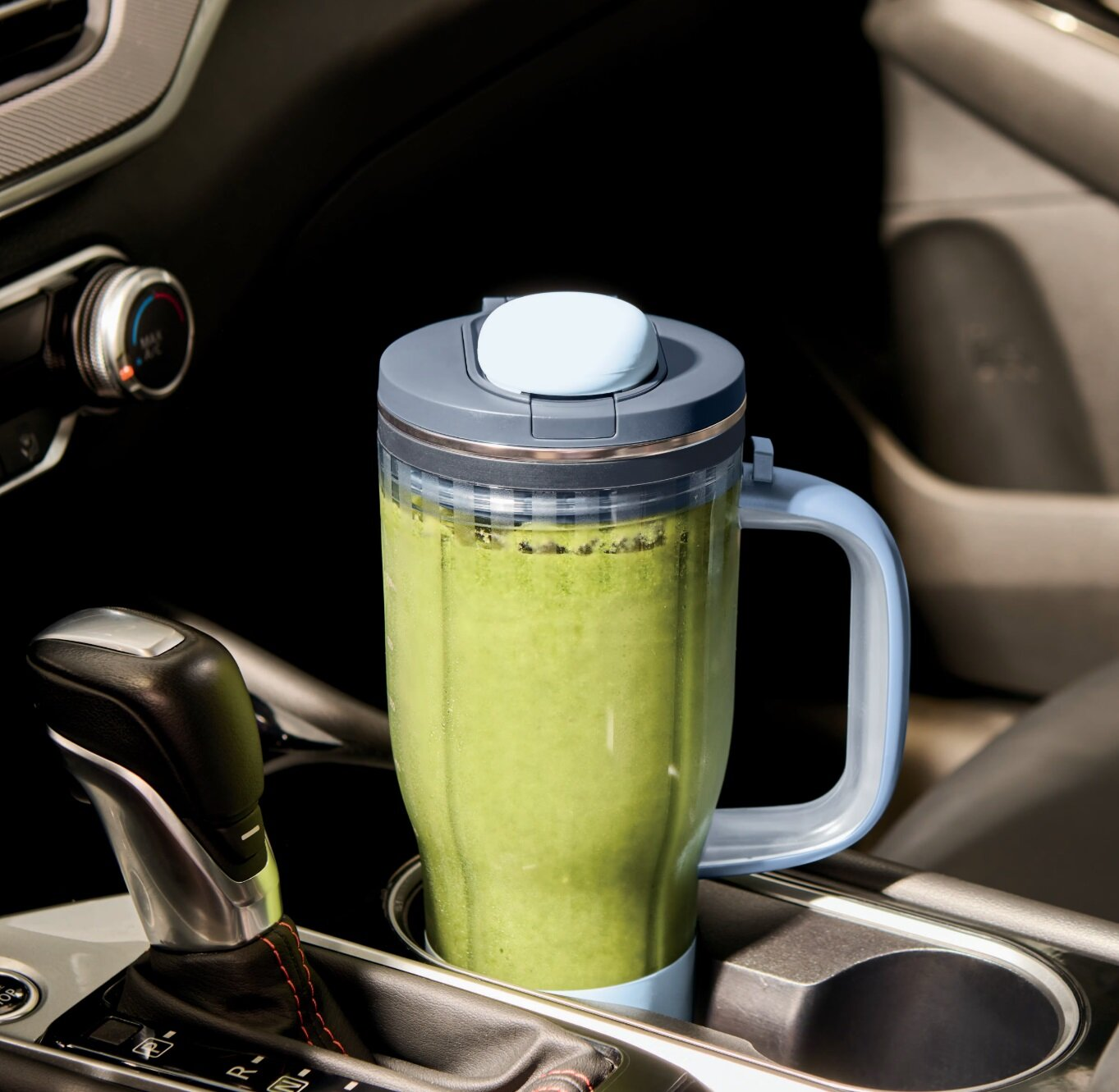 Przenośny blender z zielonym smoothie stoi w uchwycie na kubek w aucie.