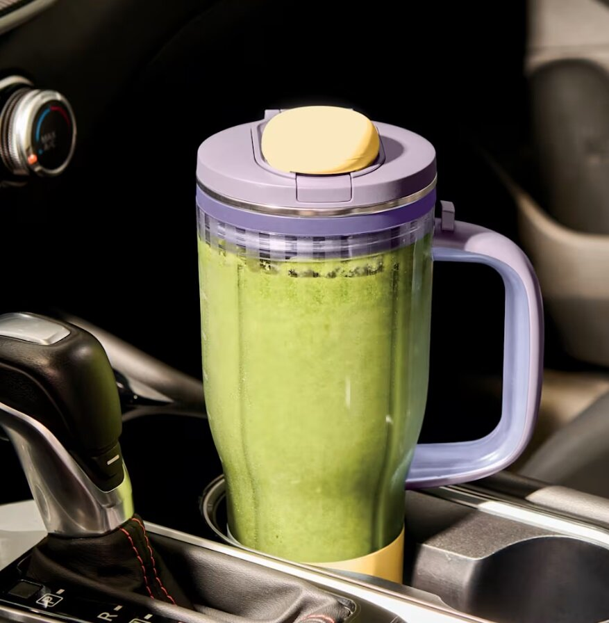 Fioletowy i żółty przenośny kubek blendera z zielonym smoothie w uchwycie na kubek w aucie.