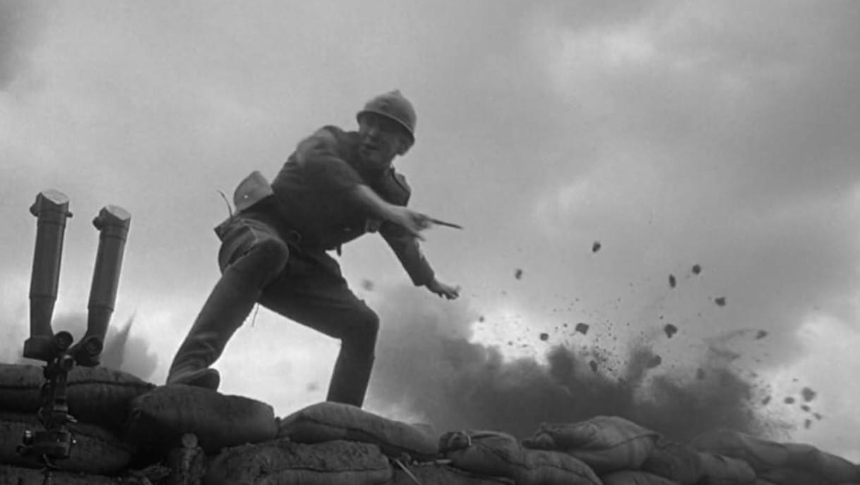 Ein Soldat in Uniform und Helm wirft eine Granate aus einem Graben hinter Sandsäcken.