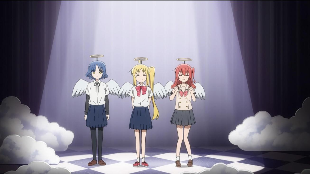 Drei Anime-Mädchen als Engel verkleidet stehen auf einer karierten Bühne im Scheinwerferlicht.