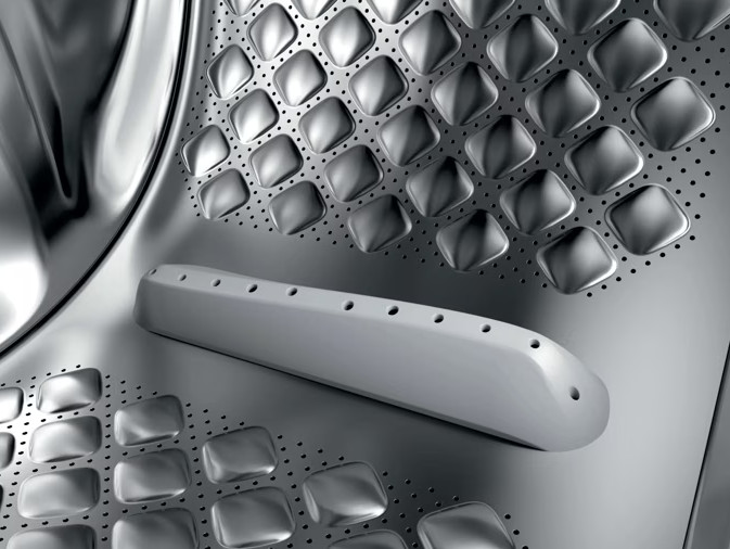 Zbliżenie błyszczącego bębna pralki ze stali nierdzewnej z wytłoczonymi poduszkami i zbierakiem.
