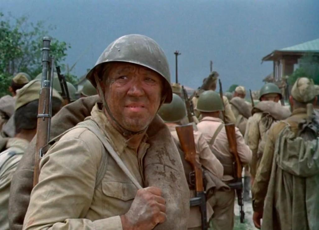 Ein schmutziger Soldat mit Helm und Gewehr marschiert in einer Gruppe.