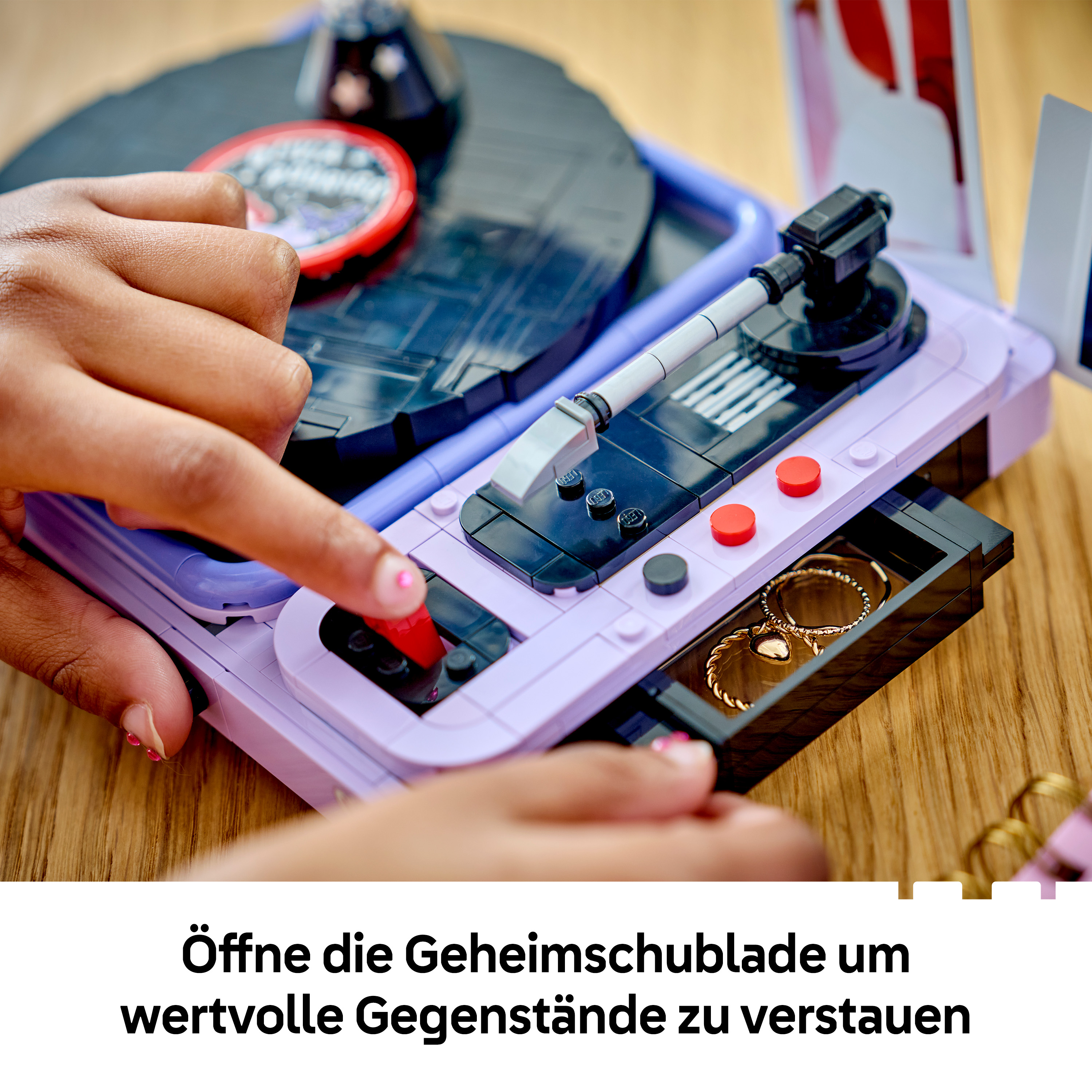 Person öffnet die Geheimschublade eines lilafarbenen Lego-Plattenspielers, in der goldene Ringe liegen.