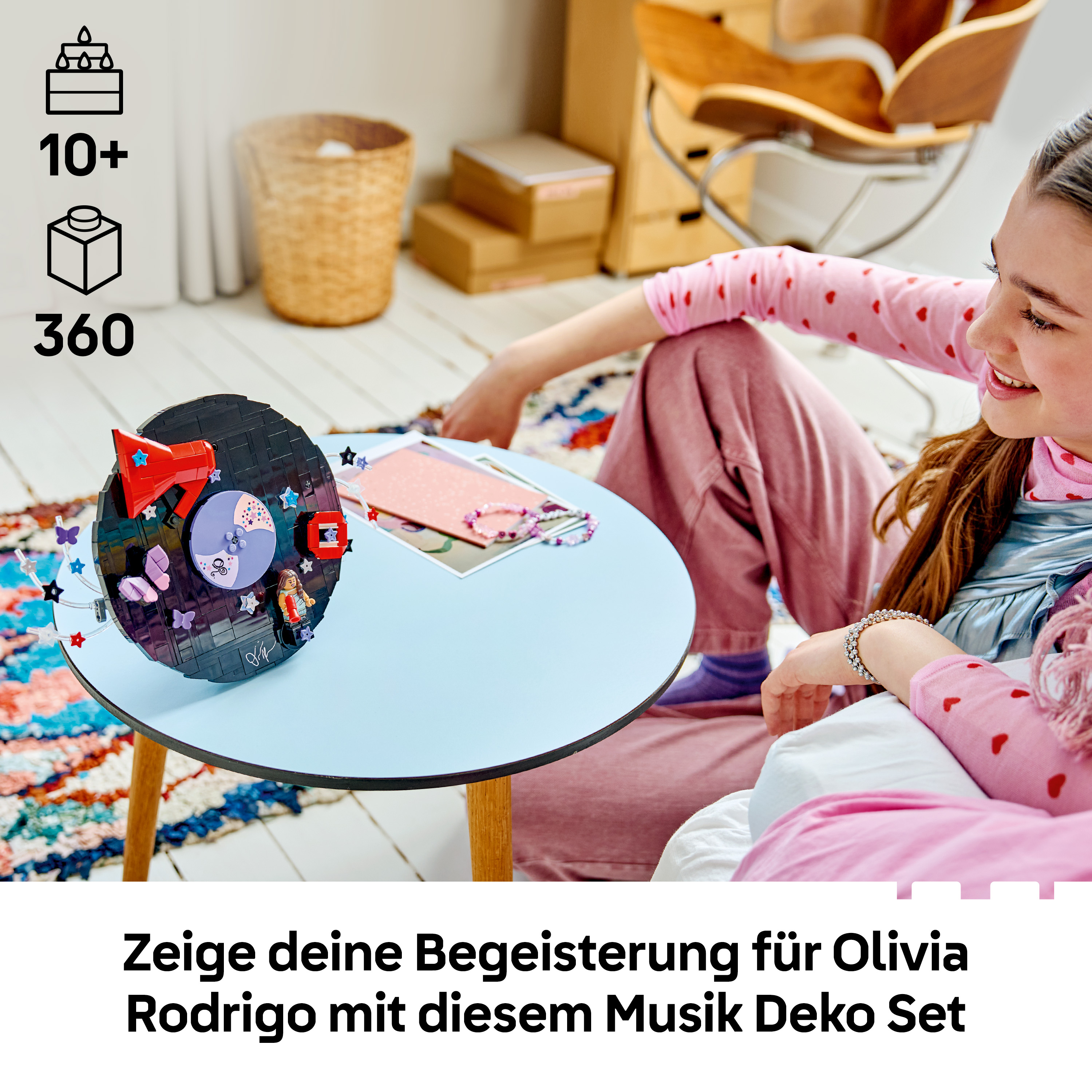 Ein Mädchen sitzt auf dem Boden und betrachtet ein Lego-Musikset auf einem blauen Tisch.