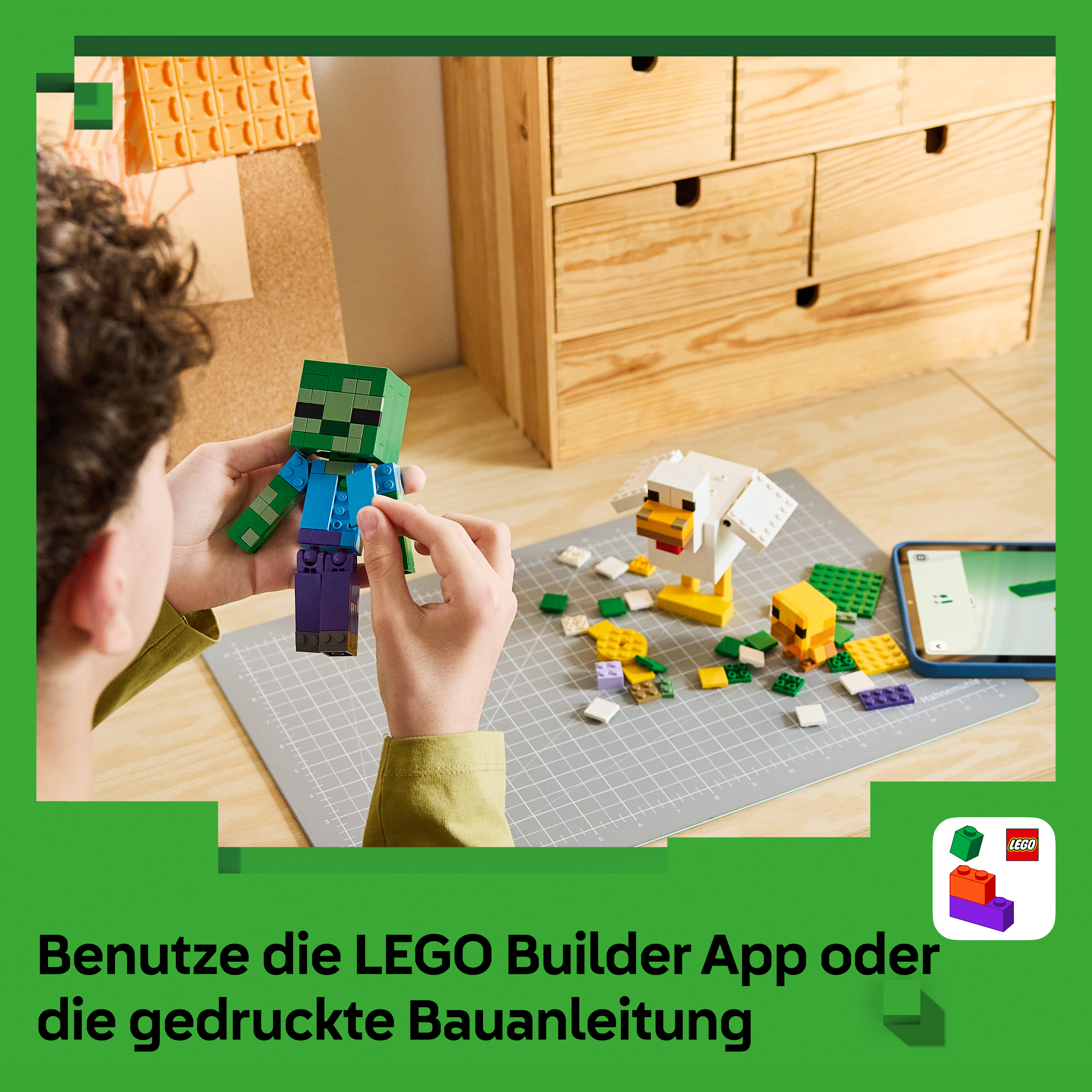 Ein Kind baut Minecraft LEGO Figuren auf einer grauen Matte, daneben ein Tablet und ein Holzzettelkasten.