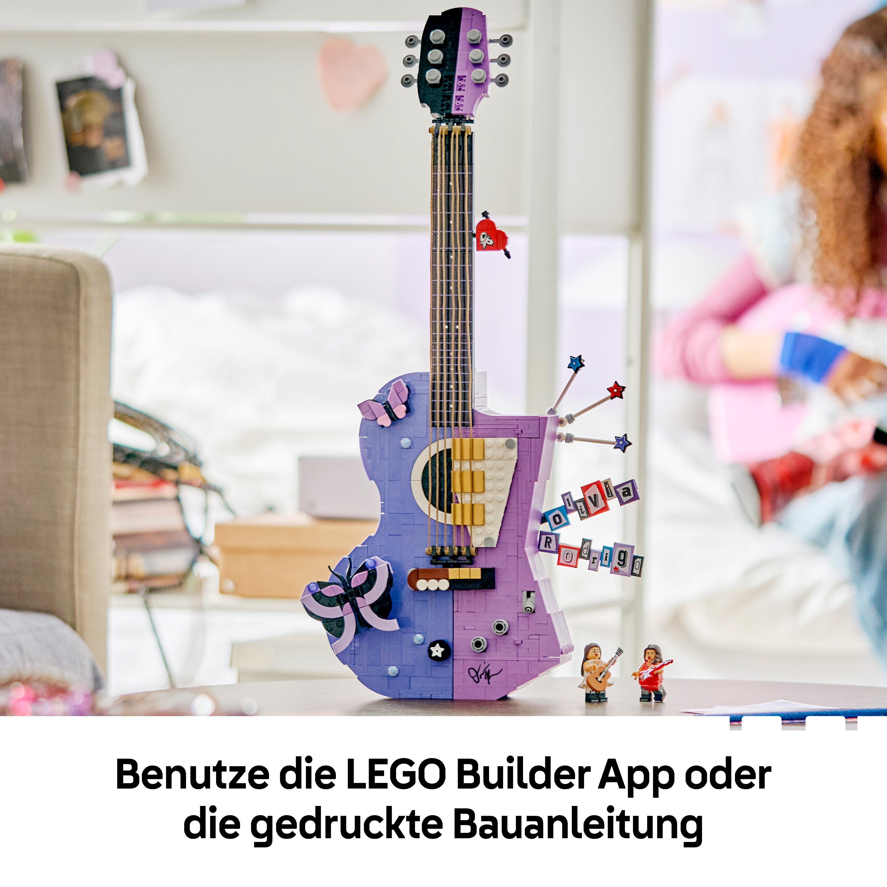 Eine violette und schwarze LEGO-Gitarre steht auf einem Tisch, umgeben von Schmetterlingen und zwei kleinen Figuren.