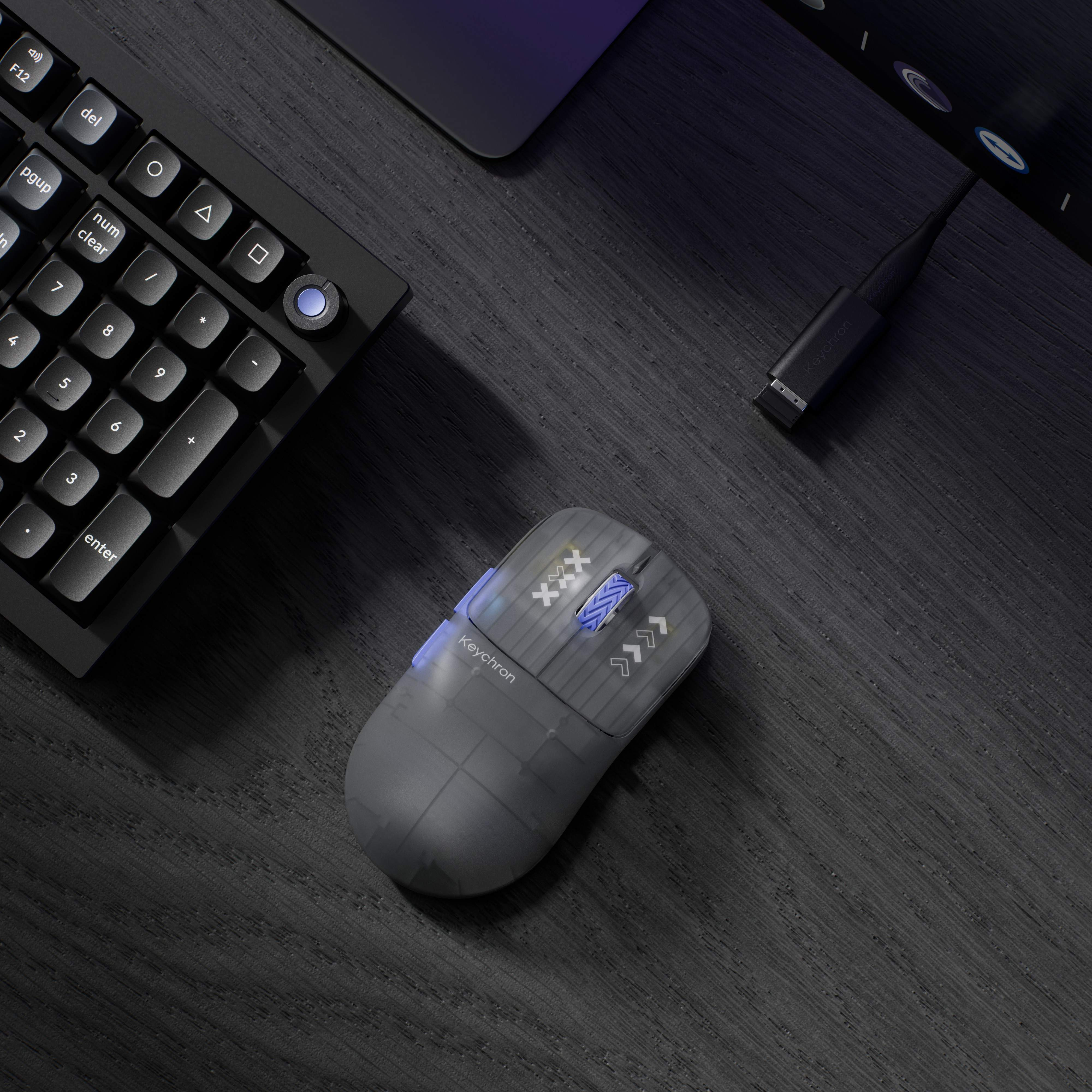 Eine graue transparente Keychron-Maus liegt auf einer dunklen Schreibtischoberfläche neben einer Tastatur.