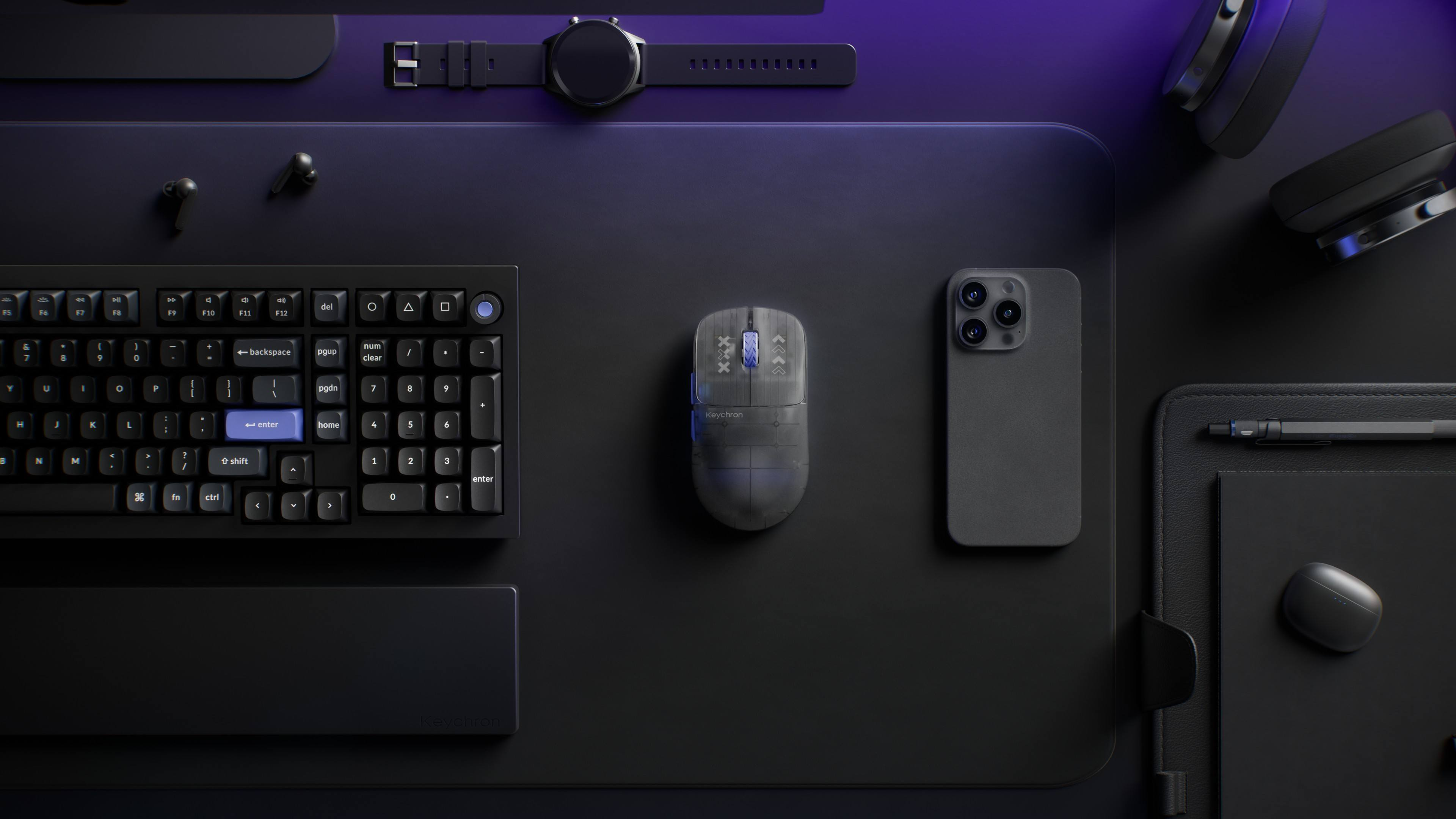 Dunkles Schreibtisch-Setup mit Tastatur, Maus, Smartphone, Kopfhörern und Uhr im Overhead-Blick.