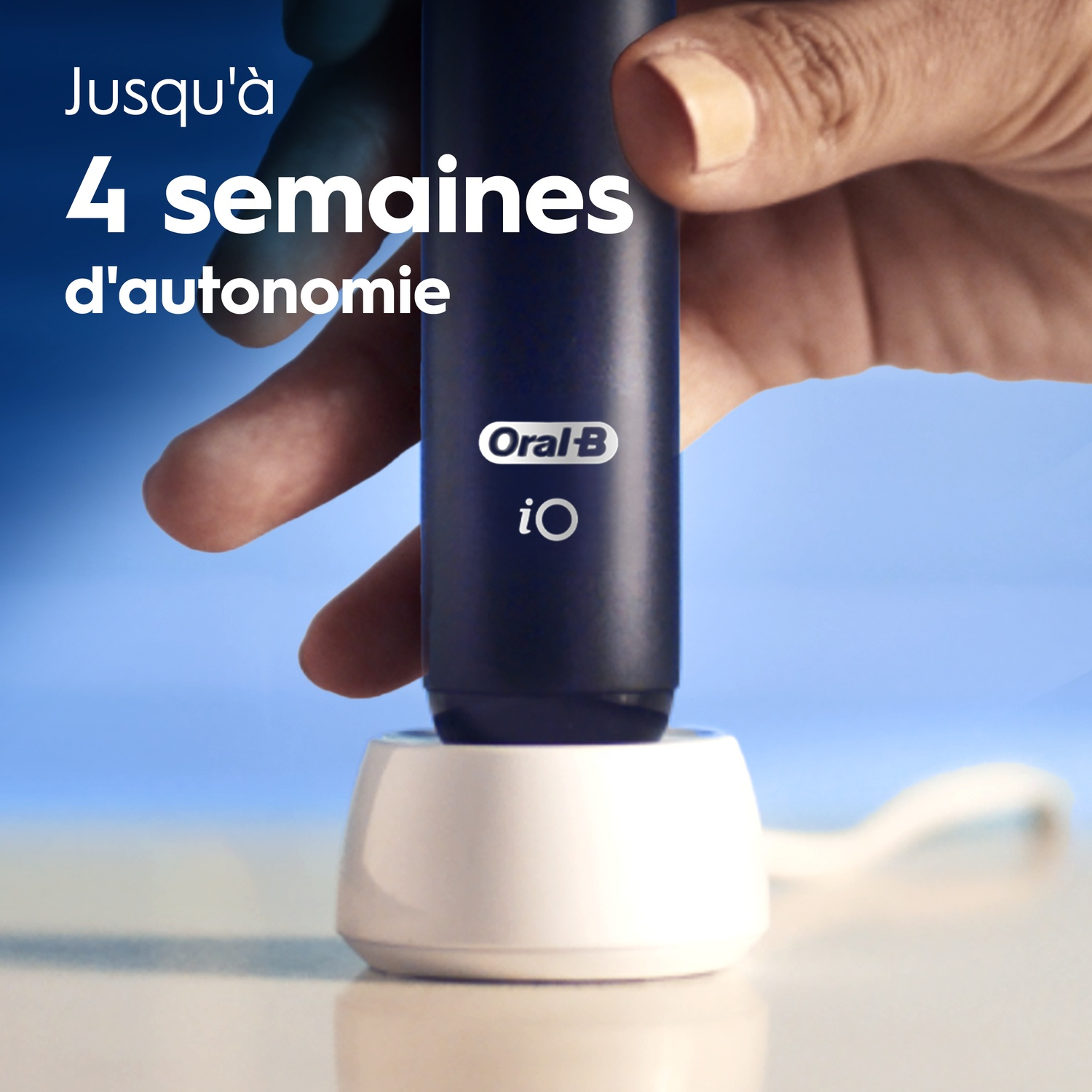 Een hand houdt een zwarte Oral-B iO elektrische tandenborstel op een witte oplader tegen een blauwe achtergrond.